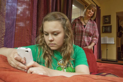 mom-looking-over-shoulder-of-girl-on-cell-phone
